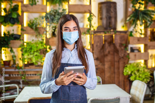 Happy female waitress using digital tablet while wearing protective face mask at the restaurant or cafe. Open again after lock down due to outbreak of coronavirus covid-19, New normal