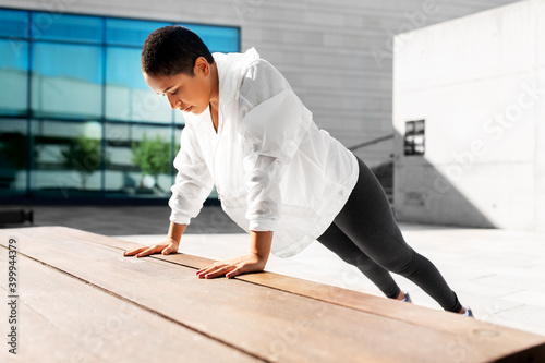 fitness, sport and healthy lifestyle concept - young african american woman doing bench push-ups at outdoors