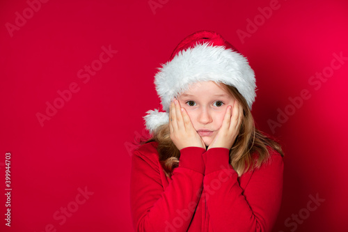 school girl with Santa Claus hat and red sweater in front of red background