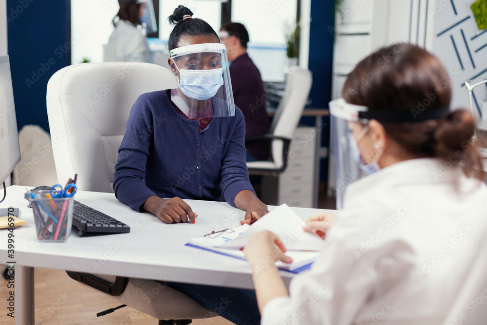 African manager pointing at finanial analysis on clipboard wearing face mask against covid19. Multiethnic team working in company with new normal respecting social distance because of global pandemic African manager pointing at finanial analysis on clipboard wearing face mask against covid19. Multiethnic team working in company with new normal respecting social distance because of global pandemic