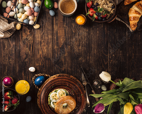 Rustic easter breakfast flat lay with eggs bagels, tulips, croissants, egg, oatmeal with berries, colored quail eggs and spring holidays decorations. Top view, copy space.