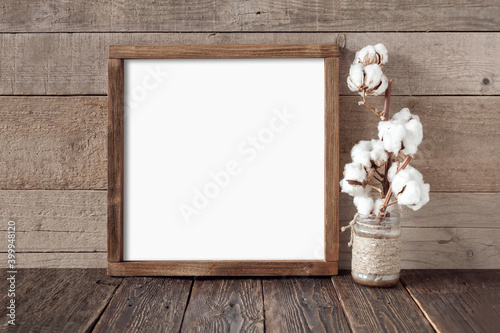 Rough square wooden frame with cotton branch on wooden background