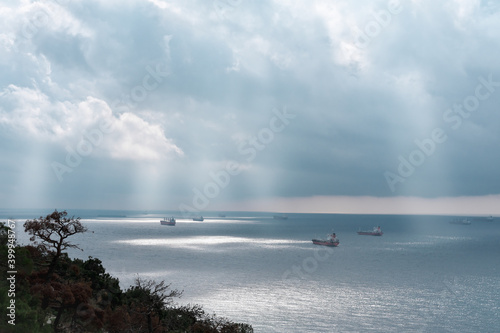 cargo ships queuing in a bay under dramatic sky. cloudy dark sky over the sea. sun light shining through the clouds.