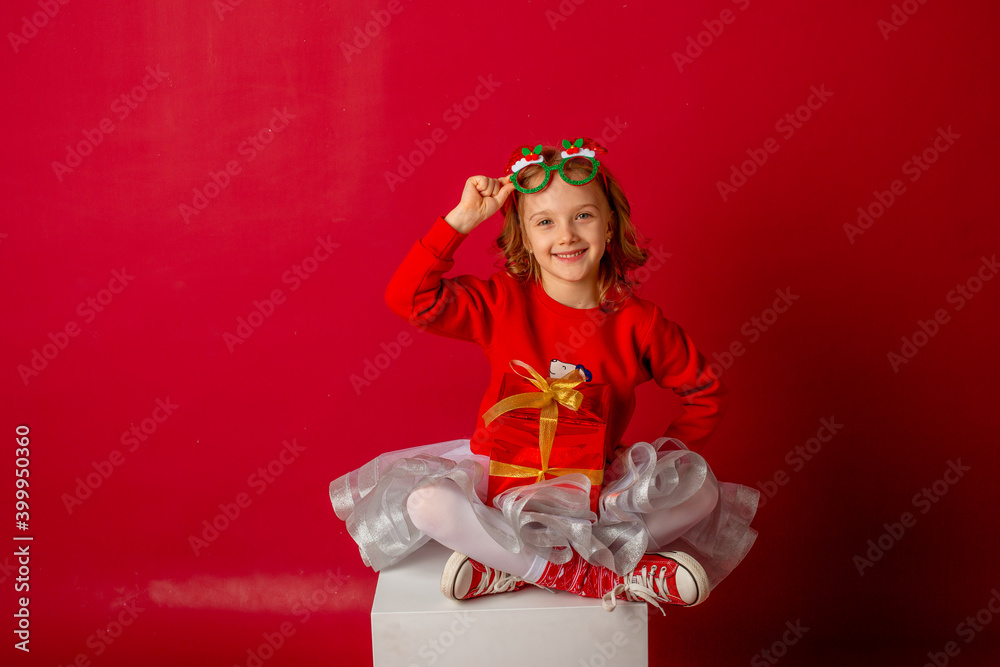 little girl in carnival glasses holds a gift on a red background, christmas little girl in carnival glasses holds a gift on a red background, christmas