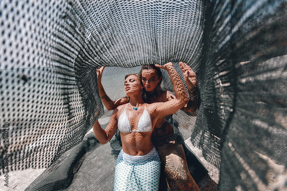 two pretty mermaids caught in a fishing net under the hot sun on the beach  Stock Photo