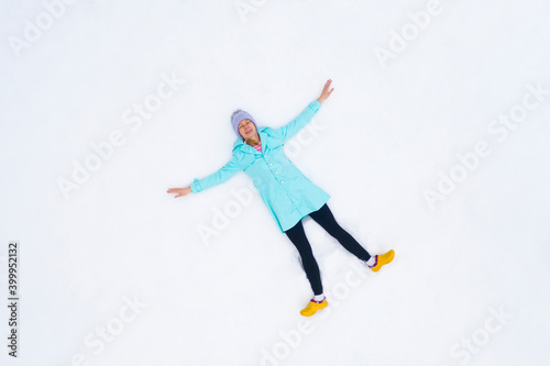 Aerial view happy woman enjoying first snow. Young happy smiling girl lying on the snow. Winter holidays and entertainment concept. Top view.