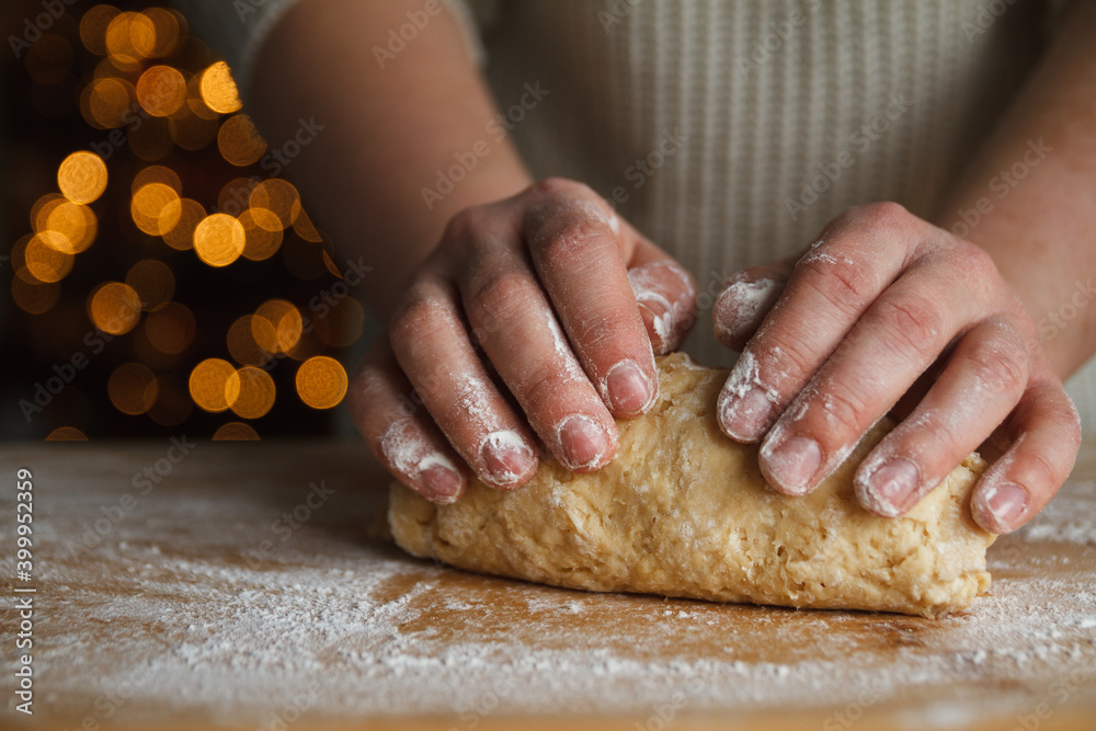 Girl kneading the dough for gingerbread cookies. Christmas tree lights bokeh in background. Female hands preparing dough, baking homemade cookies. Girl kneading the dough for gingerbread cookies. Christmas tree lights bokeh in background. Female hands preparing dough, baking homemade cookies.