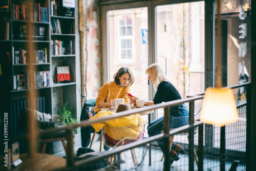 Two beautiful young hipster women friends sitting in a cafe talking and drinking coffee