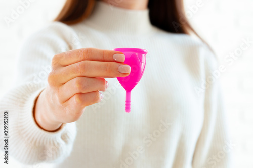 Woman in white sweater holding pink menstrual cup in hands close up