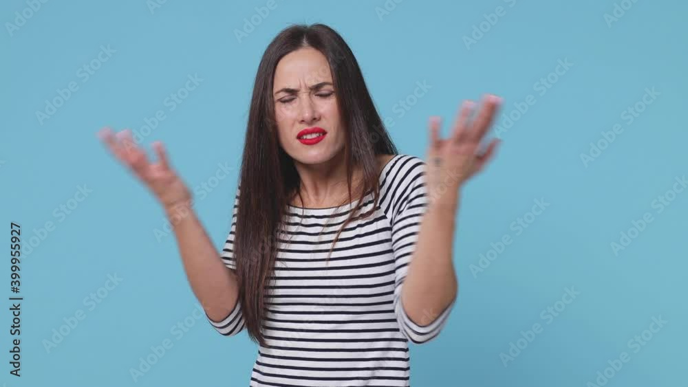 Side profile view of irritated brunette young woman 20s in basic striped shirt posing isolated on blue color background in studio. People lifestyle concept. Turn around camera spreading hands swearing Side profile view of irritated brunette young woman 20s in basic striped shirt posing isolated on blue color background in studio. People lifestyle concept. Turn around camera spreading hands swearing