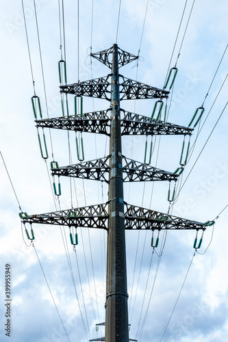 High-voltage powerful electricity tower with wires against clouds and blue sky.