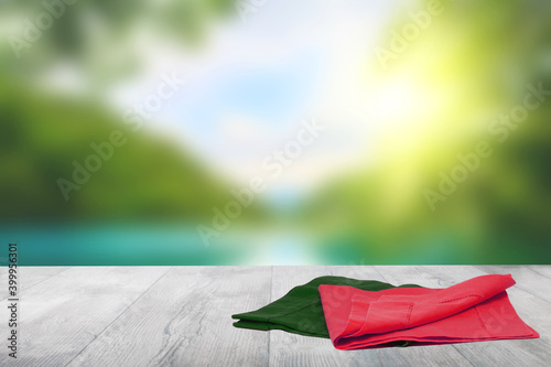 Empty table product. Closeup of a empty red and green tablecloth or napkin on a bright table over abstract blurred colorful natural background. Template for your food and product display montage.