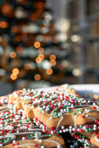 Christmas cookies with red and green in front of a blurred Christmas tree with lights. Vertical image with selective focus and copy space.