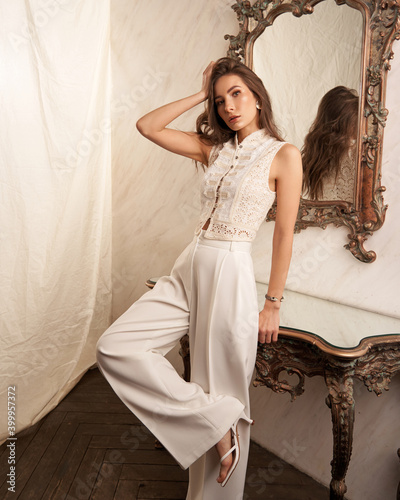 Obraz na plátně Elegant woman in white clothes standing leaning on marble table in bright interior against textile background
