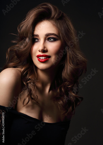 Beautiful bright makeup woman with long brown curly volume brown hair style, red lipstick, and black smokey eyes looking sexy. Closeup