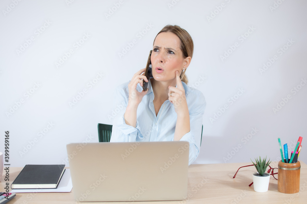 Good business talk. Cheerful young beautiful woman talking on mobile phone and using laptop while sitting at her working place Good business talk. Cheerful young beautiful woman talking on mobile phone and using laptop while sitting at her working place