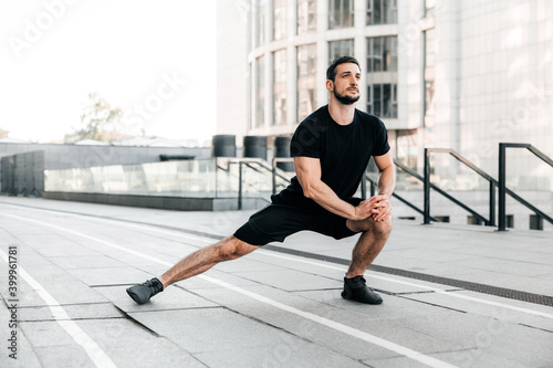 Runner doing side lunges. Portrait of sporty man doing stretching exercises before training. Male athlete preparing for jogging outdoors. Sport active lifestyle concept. Full length.
