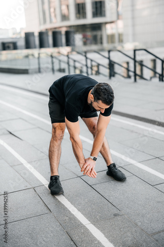 Fit man stretching back before jogging. Urban sport concept. Male runner stretches and warms up before jogging. Morning activity concept. Gray city on background.