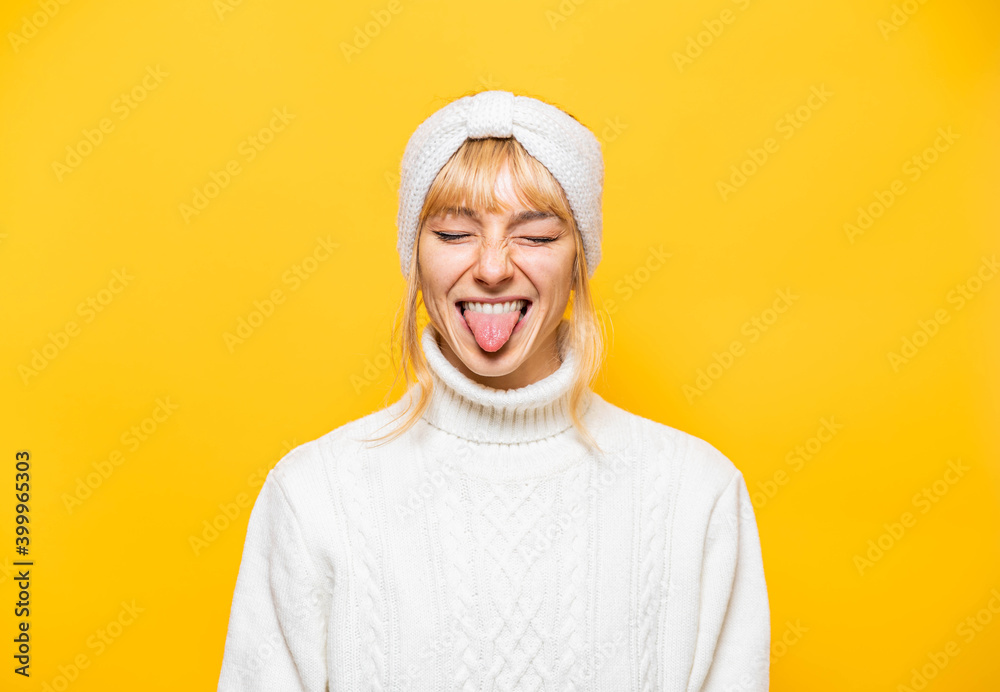 Closeup portrait of joyful funny young woman with tongue out in white comfortable clothing isolated on bright yellow background Closeup portrait of joyful funny young woman with tongue out in white comfortable clothing isolated on bright yellow background