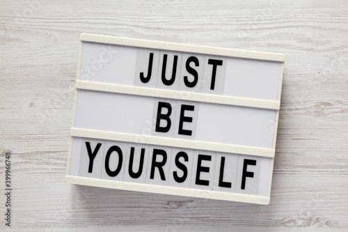 'Just be yourself' on a lightbox on a white wooden background, top view. Flat lay, overhead, from above.