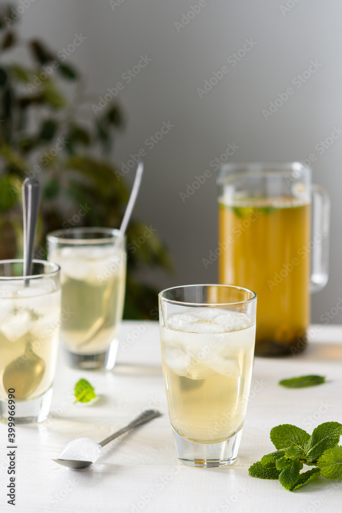 Cold refreshing green tea with ice and mint, tea jug and glasses on white wooden background Cold refreshing green tea with ice and mint, tea jug and glasses on white wooden background