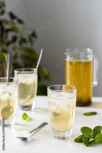 Cold refreshing green tea with ice and mint, tea jug and glasses on white wooden background