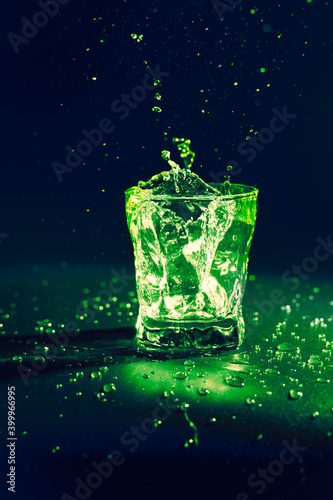 Transparent liquid colored green splashing out of glass against dark blue background