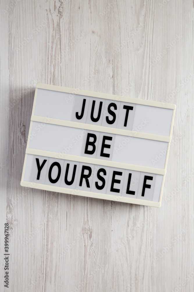 'Just be yourself' on a lightbox on a white wooden surface, top view. Flat lay, overhead, from above. 'Just be yourself' on a lightbox on a white wooden surface, top view. Flat lay, overhead, from above.