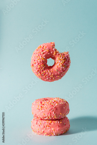 Pink donuts with colorful sprinkles with a bite flying on blue background.
