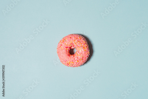Yummy pink donut with colorful sprinkles on blue background. Top view.