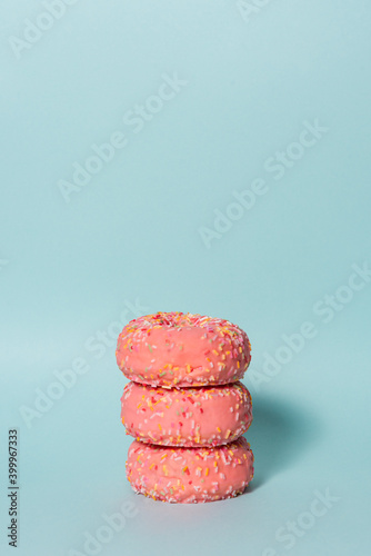 A pile of delicious pink donuts with colorful sprinkles on blue background.