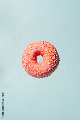 Pink donut with colorful flying sprinkles on blue background.