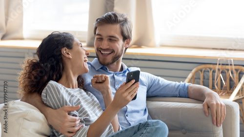Wide banner panoramic view of overjoyed millennial couple celebrate online win on cellphone together. Happy young Caucasian man and woman triumph with good sale deal or promotion discount on cell.
