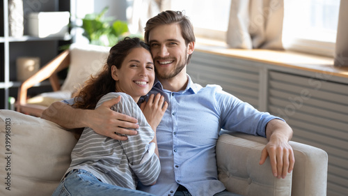 Wide banner panoramic portrait of smiling young Caucasian man and woman relax on couch in living room. Happy millennial couple renters tenants rest on sofa at home, enjoy leisure weekend together.