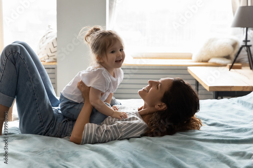 Happy young mom and small toddler daughter lying relaxing in comfortable bed playing together. Smiling Caucasian mother feel playful have fun with little 3s girl child, rest in cozy home bedroom. © fizkes