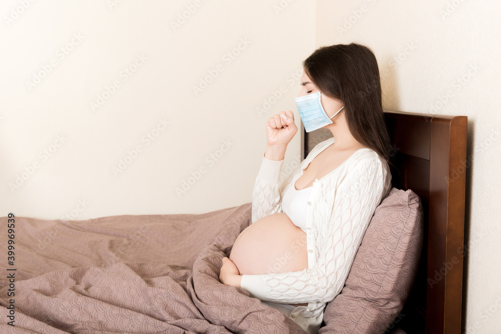 Pregnant woman in protection mask sitting on sofa. COVID-19 Coronavirus. Prevent infection to the fetus