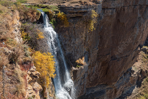Amazing narrow waterfall runs from high steep ancient limestone cliffs into deep canyon under clear blue sky on sunny autumn day