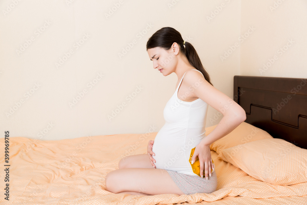Pregnant woman suffer from back pain holds a hot bottle or warmer against her back. Concept pregnant woman lifestyle and health care