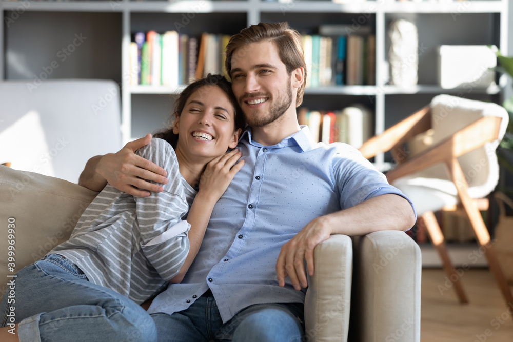 Φωτογραφία Happy young Caucasian couple sit rest on sofa hugging and cuddling, look in distance dream of future together