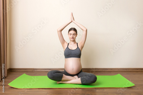 Fototapeta Naklejka Na Ścianę i Meble -  Pregnant woman exercising on green mat in room. Pregnancy Yoga and Fitness concept at coronavirus time