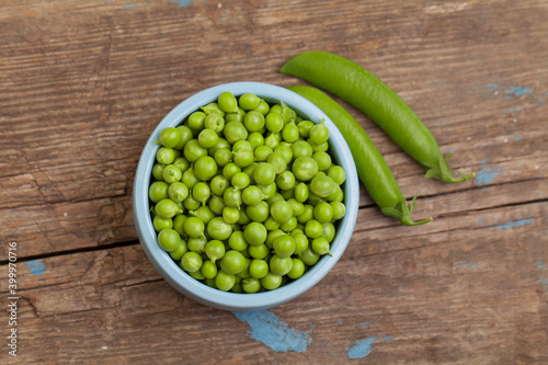 Green peas in blue bowl on vintage gray wooden table background