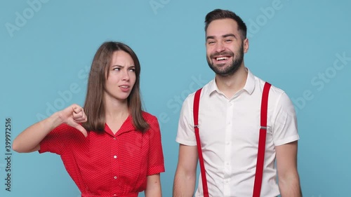 Smiling confused young couple friends bearded man woman 20s in white red clothes isolated on blue background studio. People lifestyle concept. Looking camera showing thumb up down like dislike gesture