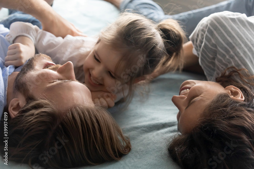 Obraz na plátně Close up of overjoyed young Caucasian parents lying in bed have fun play with little daughter