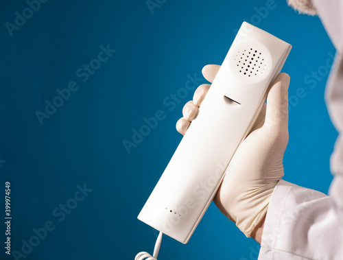 Phone in the hands of a doctor with sanitary gloves, (attention and telephone assistance), with a blue background