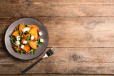 Delicious persimmon salad served on wooden table, flat lay. Space for text