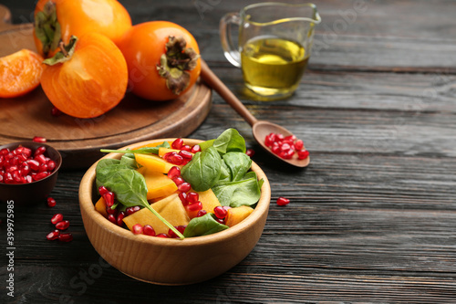 Delicious persimmon salad with pomegranate and spinach on wooden table. Space for text