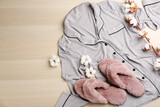 Pair of fluffy slippers, pajamas and space for text on wooden background, flat lay. Comfortable home outfit