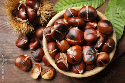 Delicious roasted edible chestnuts on brown wooden table, flat lay