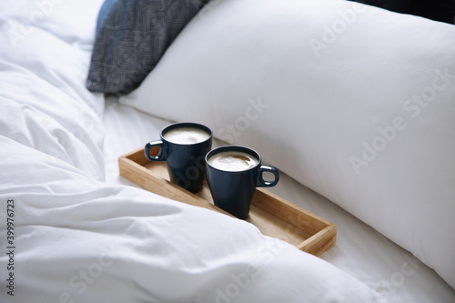 Wooden tray with cups of coffee near soft blanket on bed