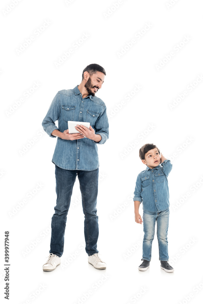 Smiling hispanic man holding digital tablet while grandson talking on smartphone on white background, two generations of men Smiling hispanic man holding digital tablet while grandson talking on smartphone on white background, two generations of men